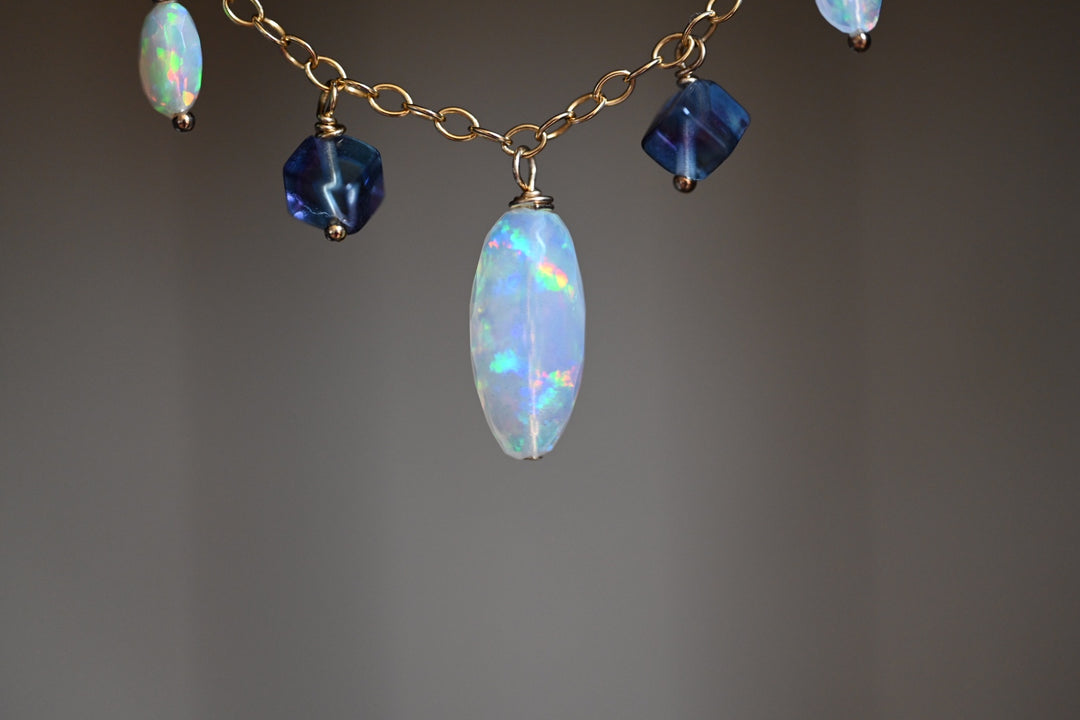 Necklace with opal and blue gemstone beads on a gray background. Delicate opal bead necklace with purple fluorite accents gold filled over sterling silver OpalOra.