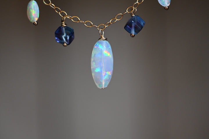 Necklace with opal and blue gemstone beads on a gray background. Delicate opal bead necklace with purple fluorite accents gold filled over sterling silver OpalOra.
