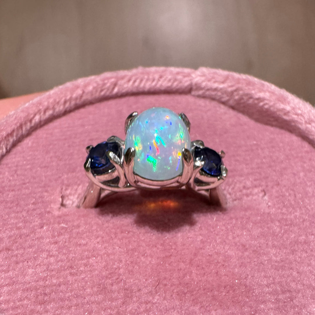 Close-up of opal gemstone with blue sapphire accents in white gold ring