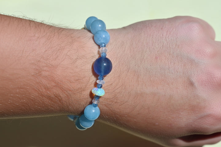 Blue beaded bracelet on a wrist against a light background. Blue gemstone bracelet aquamarine fluorite 14K yellow gold handcrafted jewelry made in USA OpalOra.