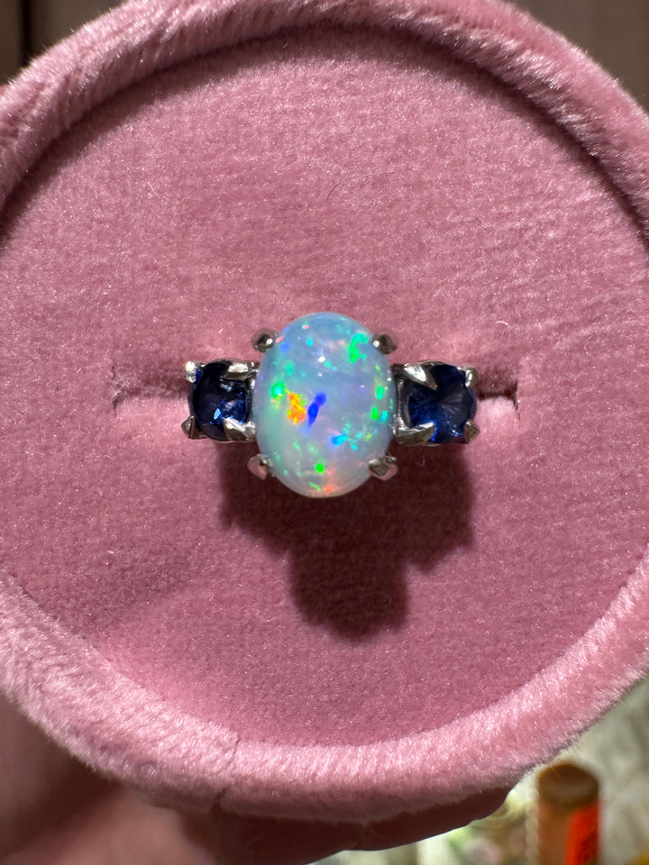 Custom opal ring showing color play and blue sapphire side stones