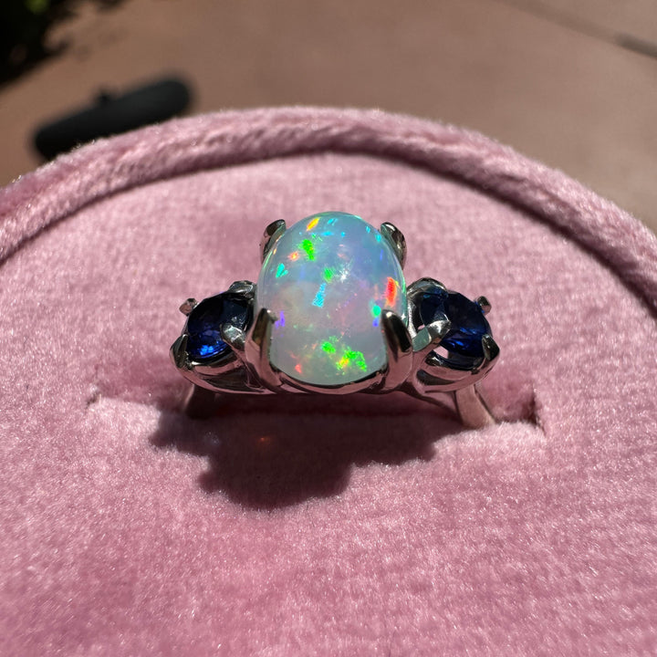 Close-up of opal gemstone with blue sapphire accents in white gold ring