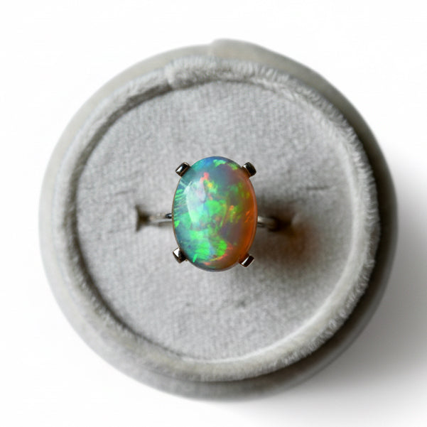 Opal ring on a gray cushion with a white background. Luxury opal ring with rare dendritic inclusions handcrafted in 14K white gold by OpalOra jewelry. 