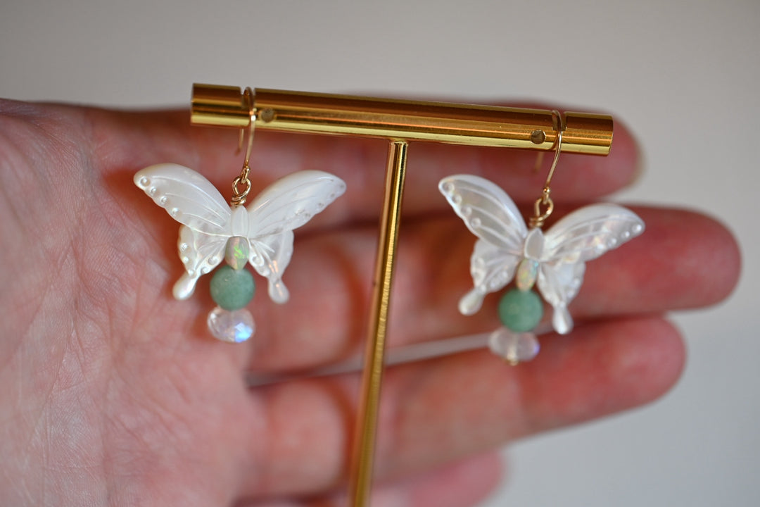 Get ready to flutter away with our exquisite 14K gold earrings featuring natural emeralds, opals, and moonstones in delicate butterfly shapes.

These beauties dangle at a length of 1 1/2 inches, perfect for adding a touch of whimsy to any outfit.
