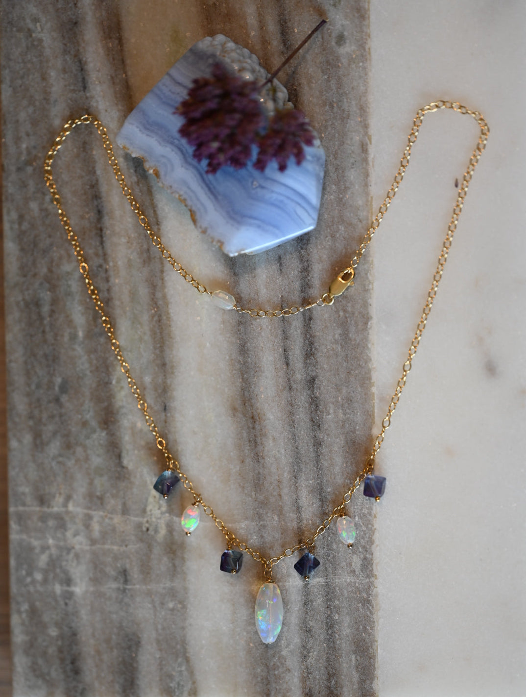 Gold necklace with gemstones on a marble surface. Luxury gemstone necklace white opal and fluorite beads on gold filled sterling silver chain made in USA.